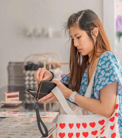 Pretty Asian woman is taking out card and cash to pay at cafe restuarant at the counter.の写真素材