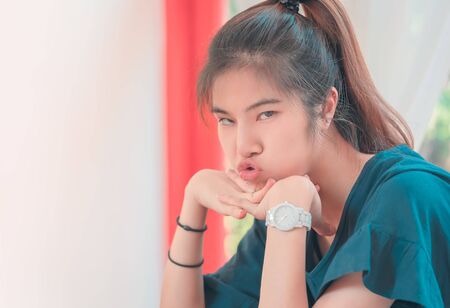 Happy chinese asian woman sitting in a coffee shop restaurant alone with kissing blowing mouthの写真素材