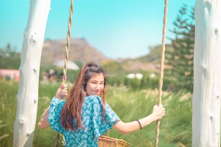 Happy beautiful Asian woman having relax time on a swing in nature field for nature hapiness lifestyleの写真素材