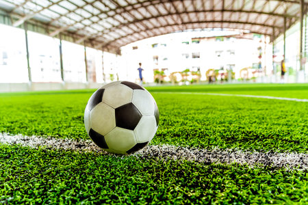 Used weared out classic black and white football soccer ball on training pitch with blur background