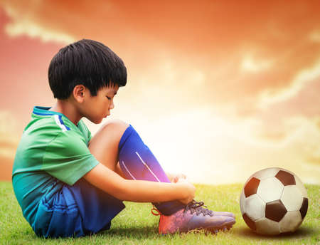 Little soccer football playing is sitting sadly with football on his side after losing a sport game.の写真素材