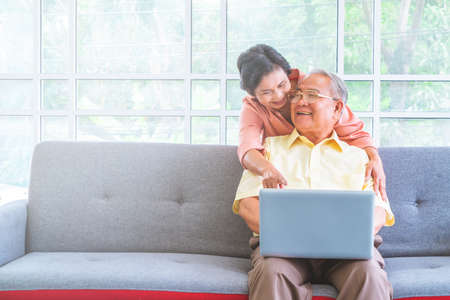 Senior couple is waving to family on Video Call communication technology on Laptop computer on a sofa at homeの写真素材