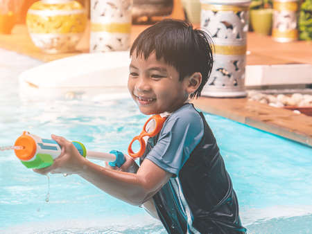 Asian Kid boy is playing with splash water gun on a swimming pool in Thailand tropical resort.の写真素材