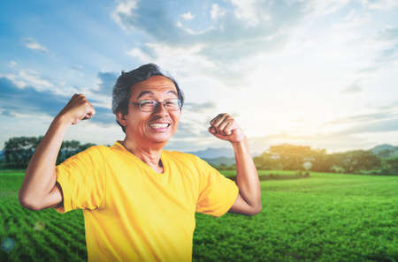 Senior Asian Man showing off muscle for strong healthy lifestye concept in a nature farming field background.の写真素材