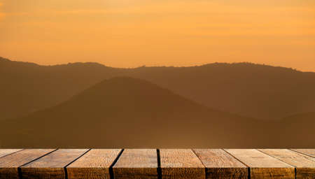 Empty display wooden board shelf counter with copy space for advertising backdrop and background with orange sunset silhouette mountain.の写真素材