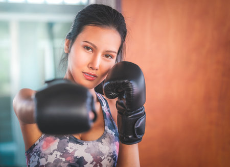 Asian woman is throwing Boxing punch into the camera in an indoor gym working out for fitness and...