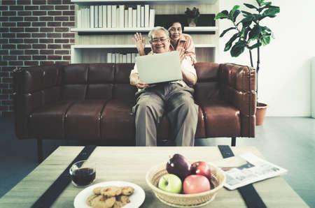 Asian Senior Elderly couple is waving to computer while using video calling technology to talk to family from home.の写真素材