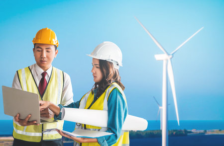 two Sustainable Energy engineer male and female is discussing on document plant with Wind turbine.