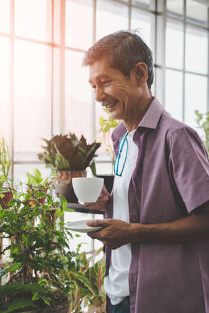 Senior Asian man having morning coffee in his houseplant garden glasshouse home.の写真素材