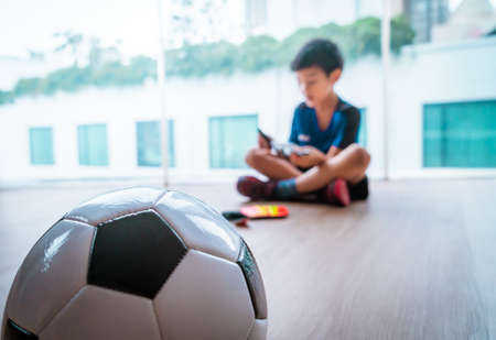Little Football goalkeeper boy is sitting and relaxing with soccer ball on the foreground.の写真素材