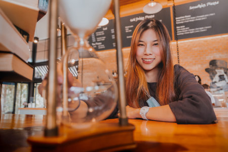 Beautiful asian young female is sitting before a hourglass counting down with smile for relaxing...