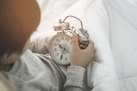 Boy wake up on his bed and looking at late alarm clock in the morning.の写真素材