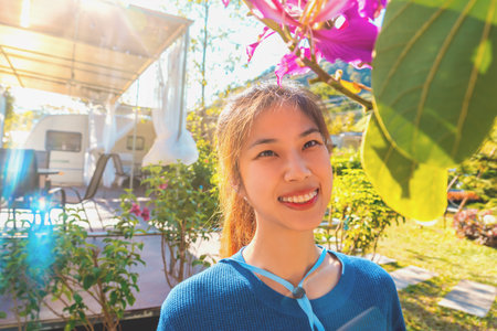 Beautiful Asian woman is looing at pink flower in the garden caravan camping with sunlight setting.の写真素材