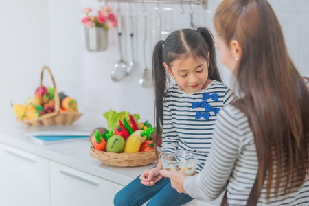 Mother is feeing child with cereal on kitchen counter for breakfast with vegetable and ingredient on background.の写真素材