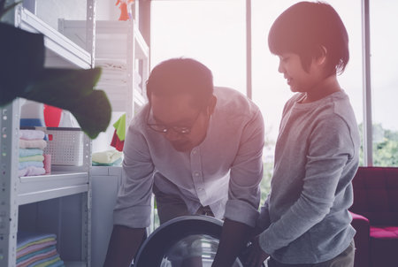 Asian Father with his son is doing laundry in washing machine at home together for family housework togetherness concept.の写真素材