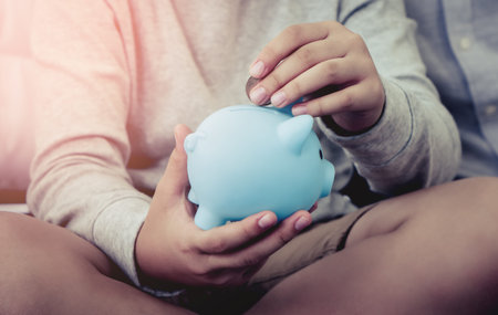 Child hand is inserting a coin into his blue piggy Bank for Kid financial Education concept.