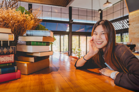 Happy Asian Woman realxing in Library cafe is smiling with many books on the table for Happy...