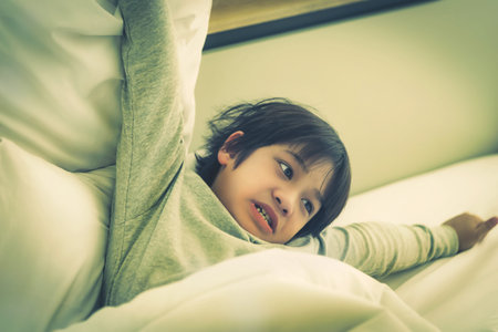 Asian boy is strecthing out on bed after wake up in the morning, with tired expression after...