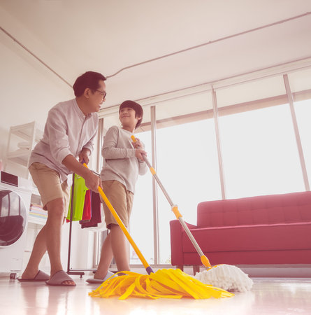Happy Asian Father and Son is using mops to clean the house floor together for family housework...