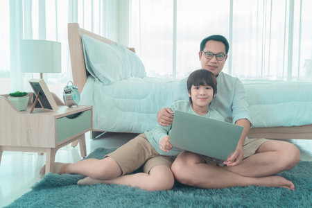 Happy Father and son is using Computer Laptop for Education together at home is the Bedroom.の写真素材
