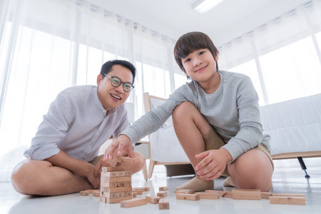 Father is teaching his son by playing with Wooden toy block tower at home together, for family home education concept.の写真素材