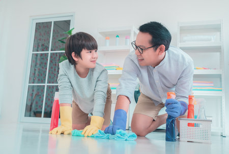 Father and son is having fun wiping and cleaning the floor together with cleaning liquid agent and colorful towels for family housework duty concept.の写真素材