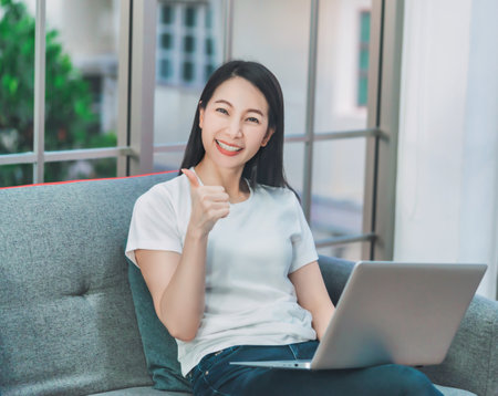 Happy Woman working on laptop in livingroom at home with ralaxing and smile during quarantine period, for new normal work from home concept.の写真素材
