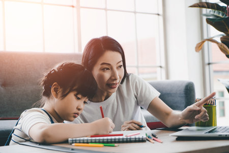 Asian Moter is helping her daughter doing homework in online education on internet on laptop during quarantine period in New normal online education concept.の写真素材