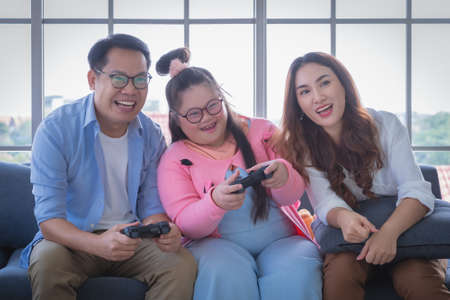Asian Family with Down Syndrome daughter playing Video game together in living room at home for Autism positive family concept.の写真素材