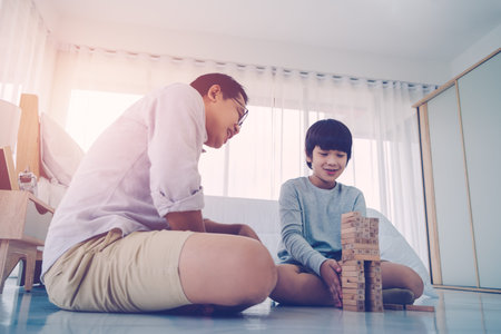 Father is teaching his son by playing with Wooden toy block tower at home together, for family home education concept.の写真素材
