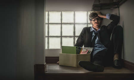 Depressed Unemployed Business office worker is sitting with card box in narrow dark stair for getting fired concept.の写真素材