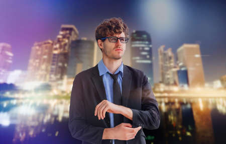 White business with glasses is touching his sleeve getting ready for work on Bangkok City night light background.の写真素材