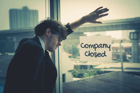 Business man standing hopeless on a sign Company closed on office windows.の写真素材