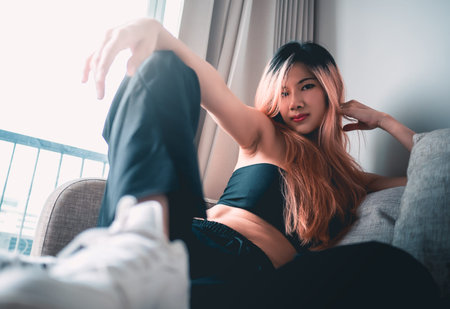 Asian Sporty Fashion model girl is posing with white sneakers shoes on Sofa in an apartment for cool...