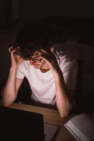 Caucasian Male with glasses worker is working on bright screen laptop computer at night with serious looking.の写真素材