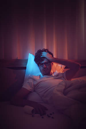 Depressed insomnia white man holding his head on a bed late at night with Black Medical pills for stress and suicide concept.の写真素材