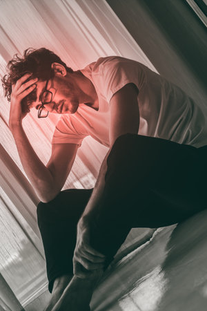 Caucasian male is sitting on the floor by the windows with depressed emotion over trouble and problem.の写真素材