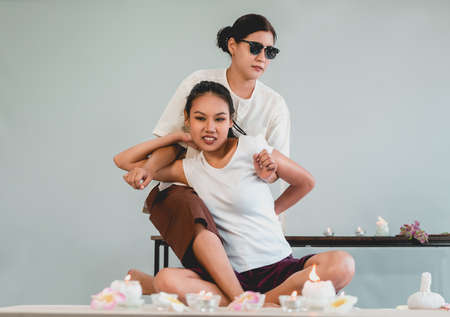 A blinded masseur Therapist is giving thai massage treatment to an Asian woman in a luxury spa, front view.の写真素材