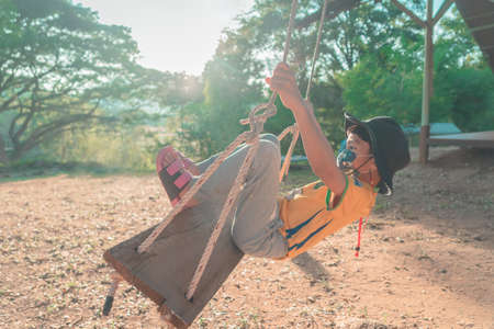 Little Boy is swinging in a campingground swing  freely, with sun and wood in the background.の写真素材