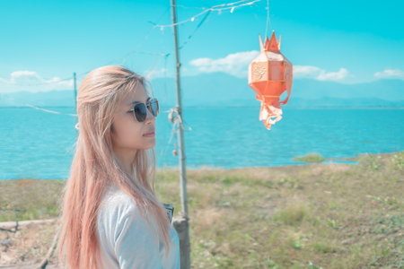 Asian young woman with sunglasses is traveling standing on a Decorated pier with Lake and mountain in the background in Phayao, Thailand.の写真素材