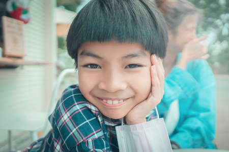 Asian boy with funny smile at the camera with mother laughing in the back.の写真素材