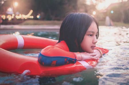 Asian pre teen girl is swimming in a floating ring in resort swimming pool in orange swimwear.の写真素材