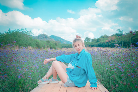 Asian woman sitting a field full of purple flower in nature with cloudy sky.の写真素材