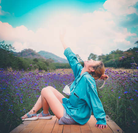 Asian woman put her hand up in sky for freedom and happiness in flower garden for relaxing and freedom conceptの写真素材