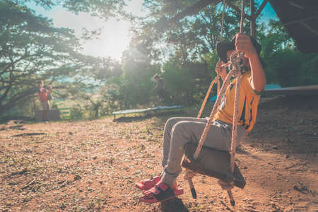 Little Boy is swinging in a campingground swing  freely, with sun and wood in the background.の写真素材
