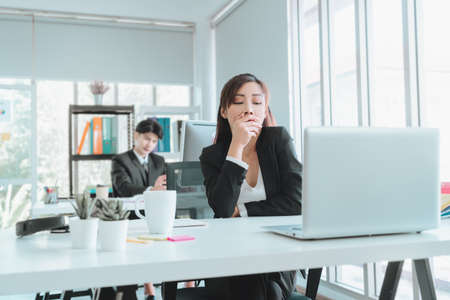 Sleepy female officer is yawning in afternoon office after tired and boredom at workplace.の写真素材