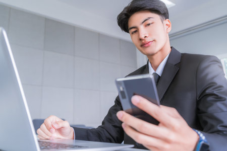 Business man is looking at mobile phone while noting down on notebook with pen.