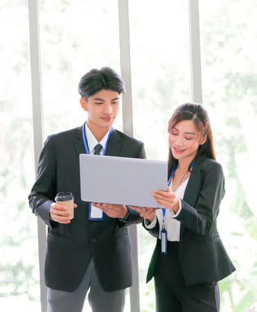 Two business person is standing while brainstorming together on a computer laptop with smile.の写真素材
