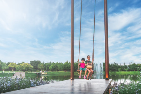 Two asian siblings is swinging on a giant swing in a public park with blue sky.の写真素材
