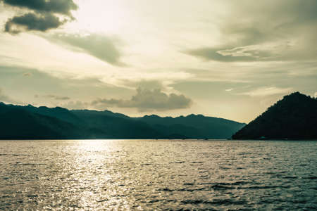 silhouette Island mountain in open water with golden sunset sky reflection.の写真素材
